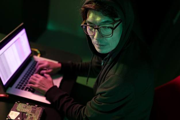 Aziatische mannelijke hacker met behulp van een laptop in de computerserverruimte. cybercriminaliteit en hackingconcept