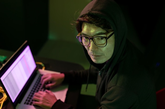 Aziatische mannelijke hacker met behulp van een laptop in de computerserverruimte. cybercriminaliteit en hackingconcept