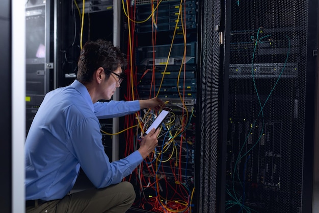 Aziatische mannelijke ingenieur die digitale tablet gebruikt en computerserver inspecteert in computerserverruimte. beheer- en onderhoudsconcept van databaseserver