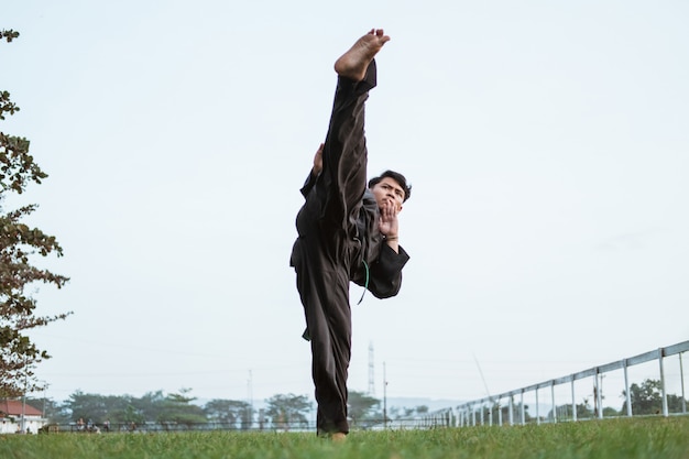 Aziatische mannelijke vechter die een pencak silat-uniform draagt, voert een rechte opwaartse trapbeweging uit