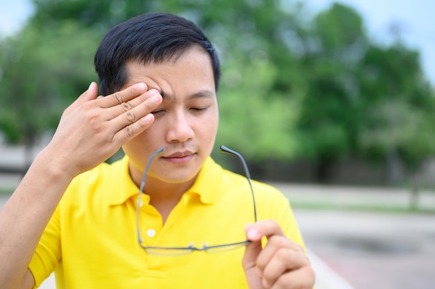 Aziatische mannen dragen gele shirts met stress, vermoeidheid van de ogen.