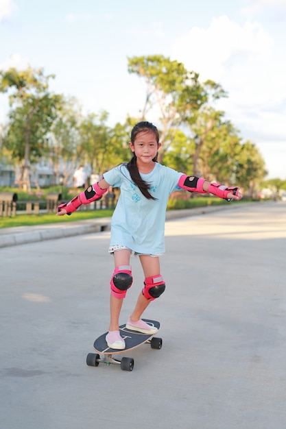 Aziatische meisje kind skateboarder dragen van veiligheid en beschermende uitrusting spelen op skateboard. Kid skateboarden op de weg buitenshuis