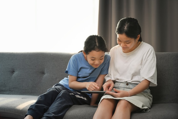 Aziatische meisjes met behulp van digitale tablet samen terwijl het aanbrengen op de bank in de woonkamer.