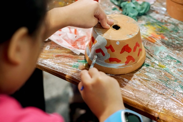 Aziatische meisjestudie en het leren van verf op bloempot in het kunstklaslokaal van haar school.