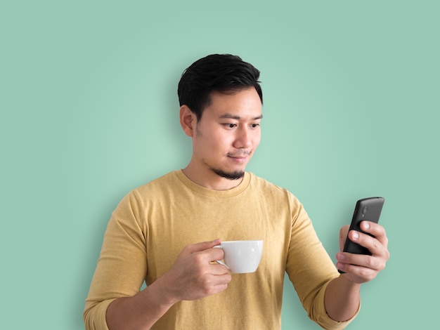 Aziatische mens die een kop van koffie heeft en smartphone gebruikt.