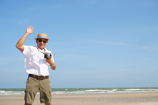 Aziatische mens die gelukkig op het strand en de blauwe tijd van de hemelzomer met uitstekende camera voelen