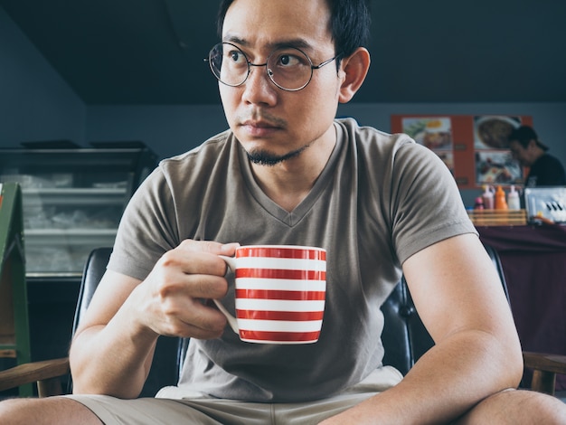 Aziatische mens die hete koffiecacao of thee op houten lijst drinkt.