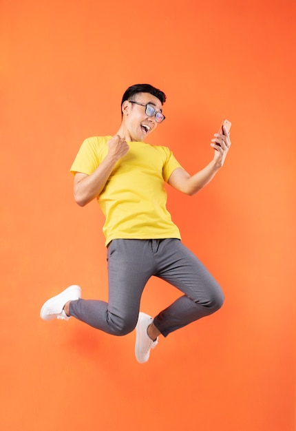 Aziatische mens die in geel t-shirt op oranje muur springt