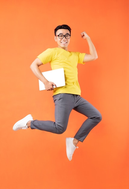 Aziatische mens die in geel t-shirt op oranje muur springt