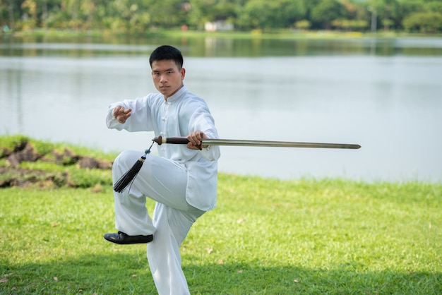 Aziatische mens die met Tai Chi-zwaard in de ochtend bij het park, Chinese vechtsporten, gezonde zorg voor het levensconcept uitwerken.