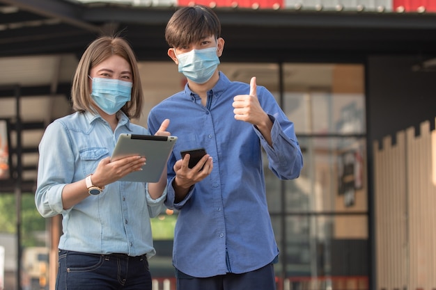 Aziatische mensen dragen een gezichtsmasker en gebruiken een tablet-smartphone op straat lopen in de stad Masker dan ter bescherming van het coronavirus covid19
