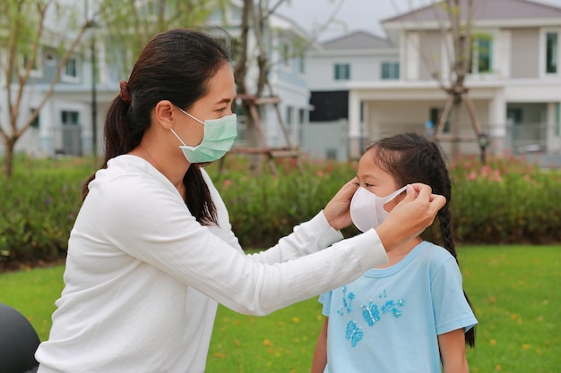 Aziatische moeder die beschermende gezichtsmaskers draagt voor dochter in tuin tijdens coronavirus en griepuitbraak