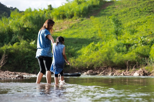 Aziatische moeder die haar kindhand houdt om samen in de rivier te lopen en te spelen