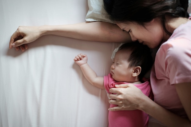 Aziatische moeder die haar pasgeboren babyslaap in bed kussen.
