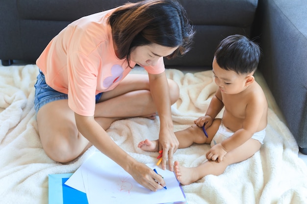 Aziatische moeder die haar schattige babyjongen leert kleurpotloden te gebruiken