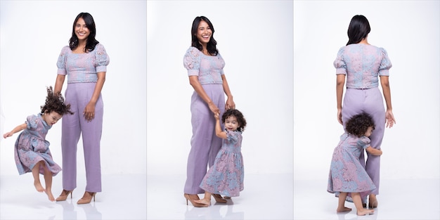 Aziatische moeder en blanke dochter staan en dragen samen dezelfde paarse blousebroekjurk. Klein meisje houdt de hand van de moeder vast en glimlacht met liefde. Witte achtergrond geïsoleerd