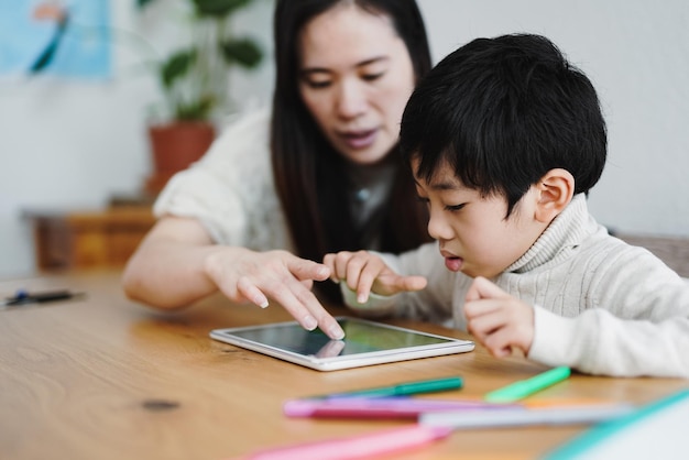 Aziatische moeder en kind leren met digitale tablet binnen - concept voor kinderopvang en technologie