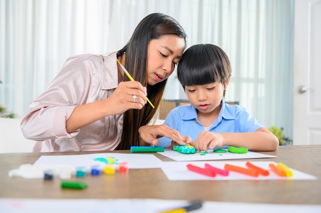 Aziatische moeder werkt thuis samen met zoon. Moeder en kind spelen deeg. Kind dat kleimodel van plasticine maakt. Vrouw levensstijl en gezinsactiviteit.