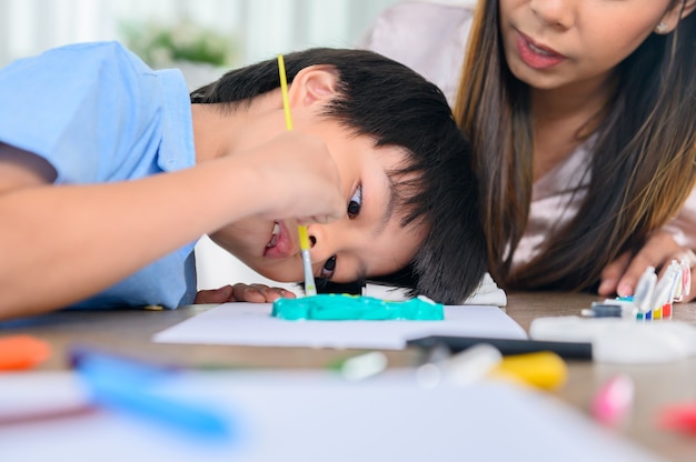 Aziatische moeder werkt thuis samen met zoon. Moeder en kind tekenen foto en kleur schilderen kunst. Vrouw levensstijl en gezinsactiviteit.