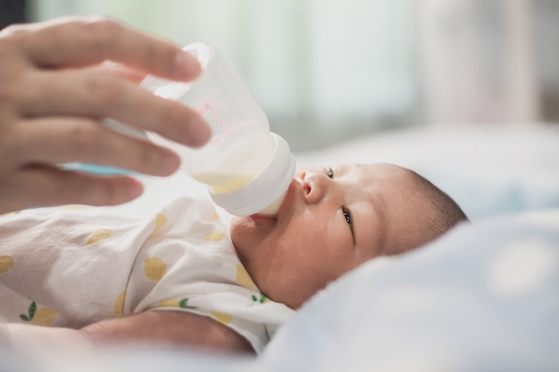 Aziatische moeder zuigfles melk aan pasgeboren baby schattige zoon in een slaapkamer.