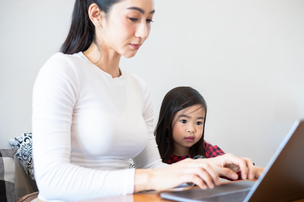 Aziatische moeders leren hun dochters thuis een boek te lezen en notitieboekjes en technologie te gebruiken voor online leren tijdens schoolvakanties. Educatieve concepten en activiteiten van het gezin