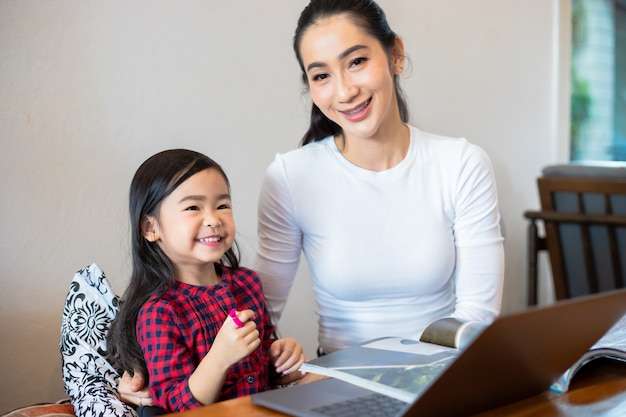 Aziatische moeders leren hun dochters thuis een boek te lezen en notitieboekjes en technologie te gebruiken voor online leren tijdens schoolvakanties. Educatieve concepten en activiteiten van het gezin