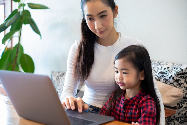 Aziatische moeders leren hun dochters thuis een boek te lezen en notitieboekjes en technologie te gebruiken voor online leren tijdens schoolvakanties. Educatieve concepten en activiteiten van het gezin