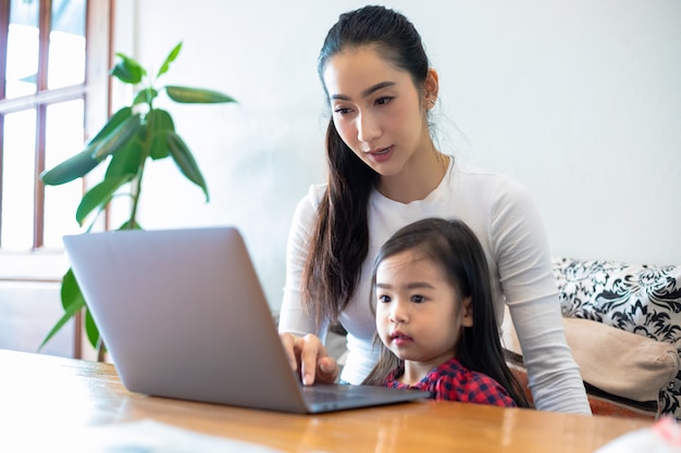 Aziatische moeders leren hun dochters thuis een boek te lezen en notitieboekjes en technologie te gebruiken voor online leren tijdens schoolvakanties. Educatieve concepten en activiteiten van het gezin