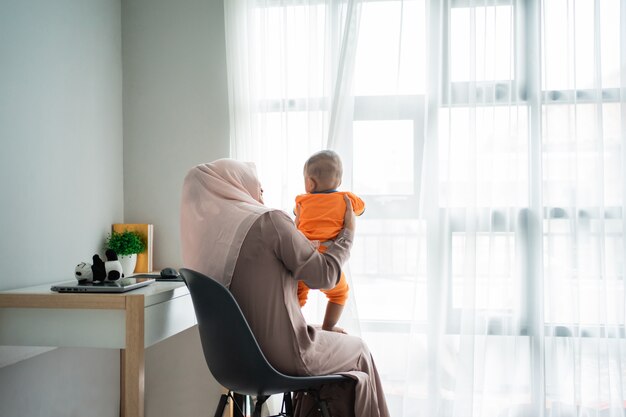 Aziatische mohammedaanse moeder die haar zoontje op schoot bij het spelen samen