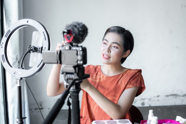 Aziatische mooie fashion beauty blogger kijkt in een digitale camera. beoordeelt schoonheidsproduct voor videoblog, praat over cosmetica die een make-uppalet vasthoudt terwijl ze haar video opneemt.