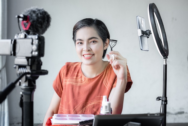 Aziatische mooie fashion beauty blogger kijkt in een digitale camera. beoordeelt schoonheidsproduct voor videoblog, praat over cosmetica die een make-uppalet vasthoudt terwijl ze haar video opneemt.