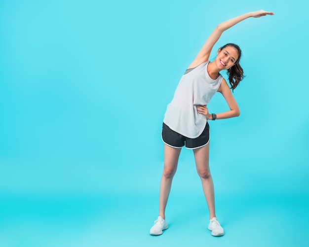 Aziatische mooie gelukkige vrouw Opwarmen en strekken lichaam voor oefening geïsoleerd op blauwe kleur achtergrond. Concept van slanke en gezonde meisje training.