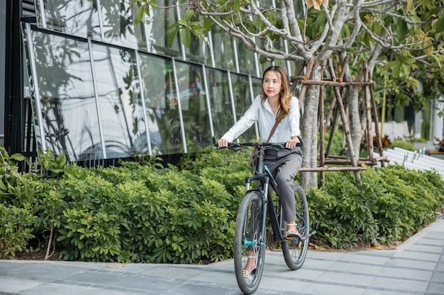 Aziatische mooie jonge zakenvrouw met helm fietsen gaan naar kantoorwerk in de stad straat met fiets in de ochtend, gelukkige levensstijl vrouw fiets na zakelijk werk buiten gebouw, eco-vriendelijk
