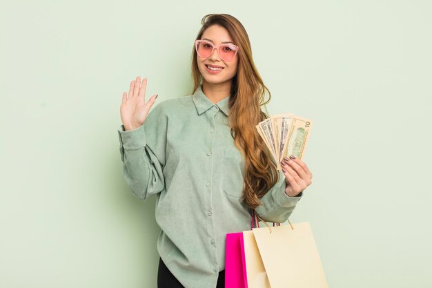 Aziatische mooie vrouw glimlachend gelukkig zwaaiend met de hand verwelkomend en groetend u boodschappentassen concept