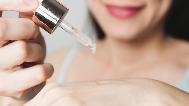 Aziatische mooie vrouw houdt druppelbuis druppel water of serum op de rug van de hand cosmetische pipet met druppels olie huidverzorging en schoonheid conceptueel