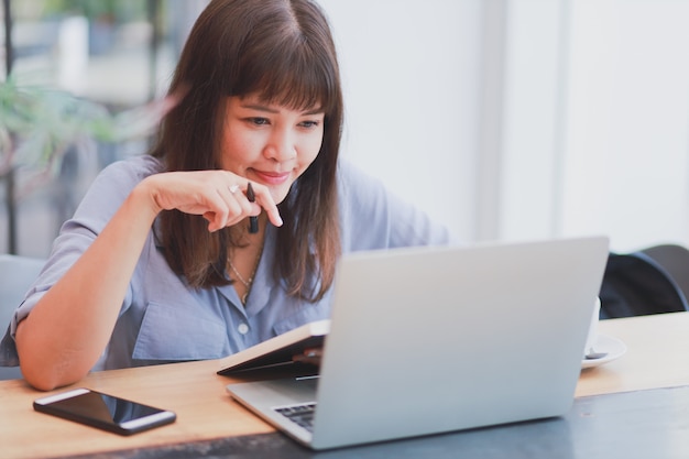 Aziatische mooie vrouw in blauw shirt met behulp van laptop en koffie drinken