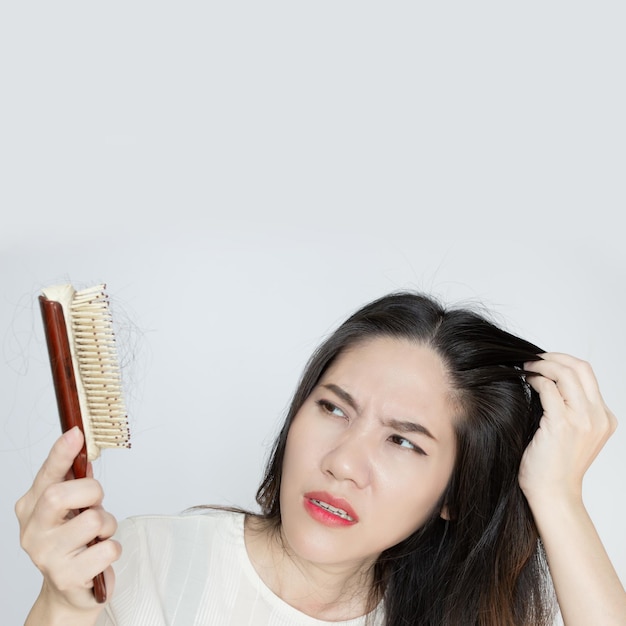 Aziatische mooie vrouw kijkt naar haar haarverlies op borstel en raakt hoofd aan met een geschokt en bezorgd gezicht