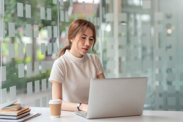 Aziatische mooie zakenvrouw zitten en werken met een laptop op kantoor.