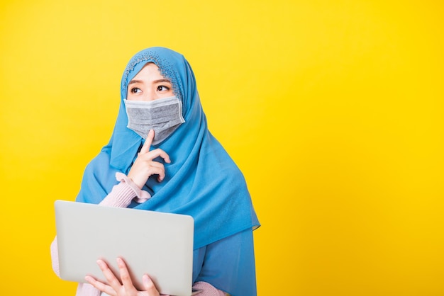 Aziatische moslim Arabier, Portret van gelukkige mooie jonge vrouw Islam religieuze slijtage sluier hijab en gezichtsmasker beschermen ze quarantaine ziekte coronavirus houd laptopcomputer vast en denkvraag