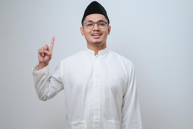 Aziatische moslim man die een vinger opstak, kreeg een goed idee en ziet er verrast uit met een glimlach geïsoleerd op een witte achtergrond