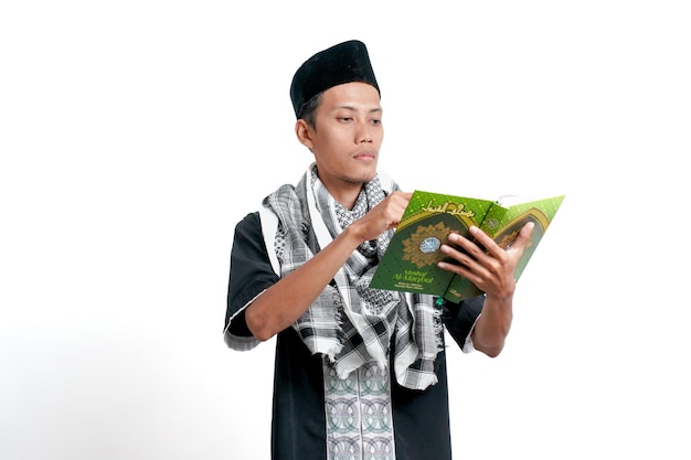 Aziatische moslim man met een moslim jurk met tulband en een pet die de koran leest geïsoleerd op een witte achtergrond