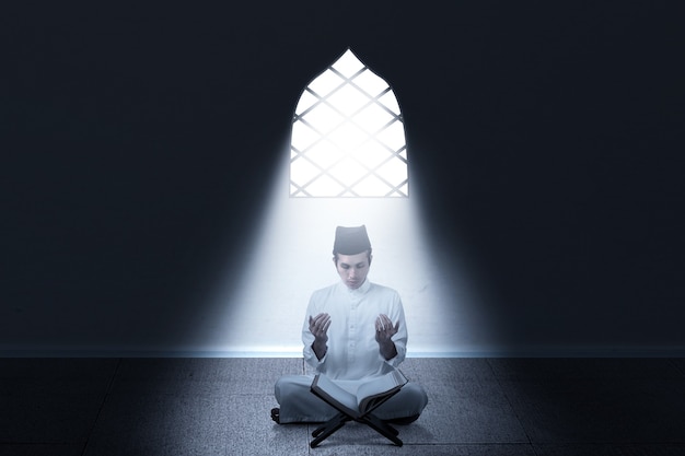 Aziatische moslim man zittend terwijl opgeheven handen en bidden in de kamer
