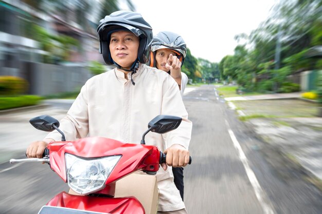 Aziatische moslimfamilie die een doos draagt op een motorfiets die mudik wordt