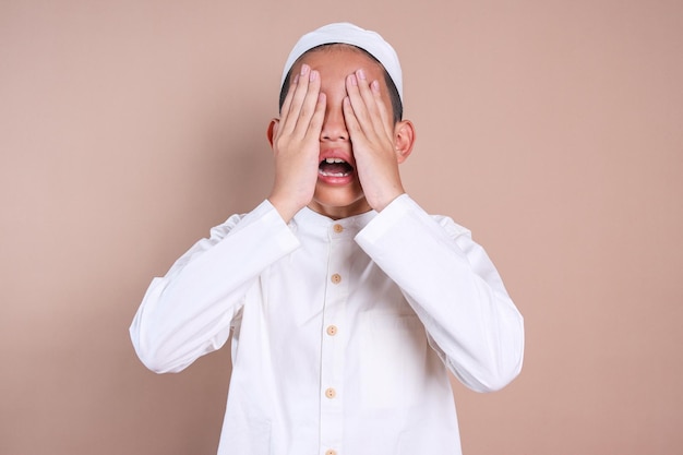 Aziatische moslimjongen die zijn oog met zijn handen bedekt.