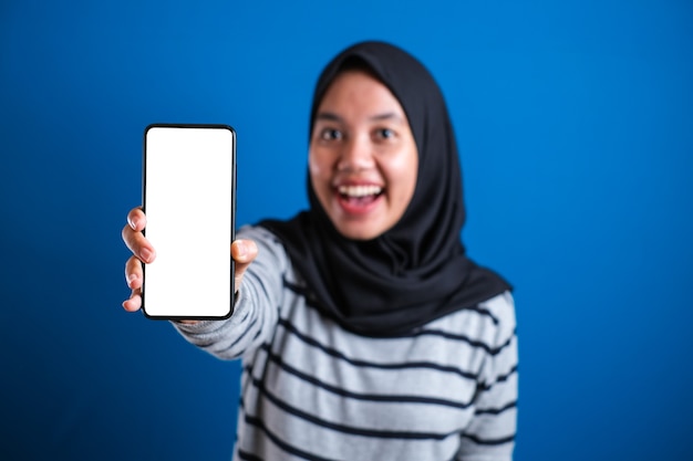 Aziatische moslimvrouw die bij camera glimlacht en haar smartphonemodel toont