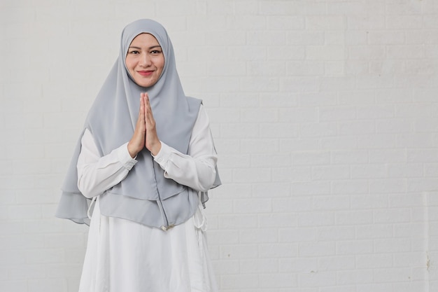 Aziatische Moslimvrouw die een hijab draagt die Eid Mubarak-groet op witte achtergrond gebaart