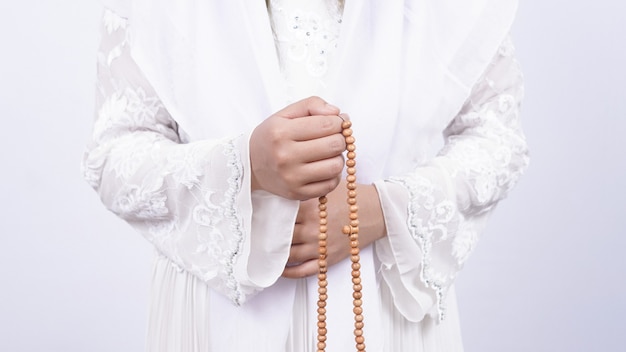 Aziatische moslimvrouw die gebedparels draagt, bidt met tasbih in het wit