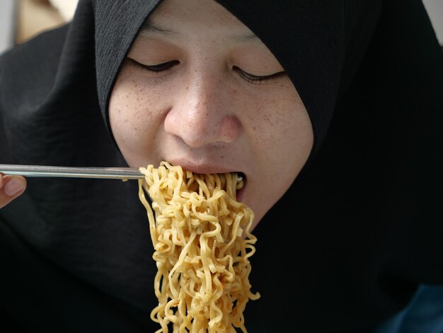 Foto aziatische moslimvrouw eet instant gebakken noedels ongezond fastfood