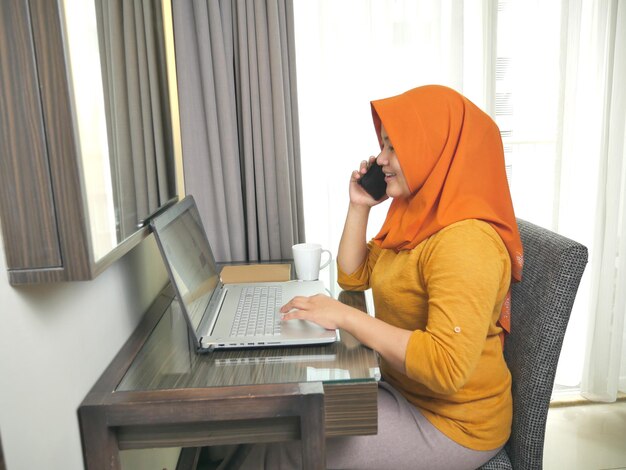Foto aziatische moslimvrouw glimlacht terwijl ze aan de telefoon praat succesvolle zakenvrouw ondernemer