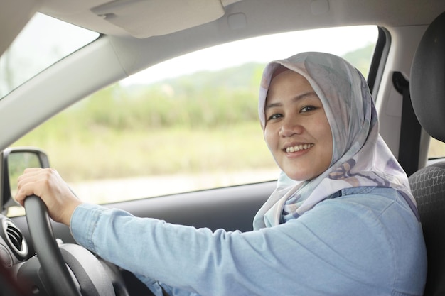 Aziatische moslimvrouw glimlacht terwijl ze met haar auto rijdt in een vakantiereis.